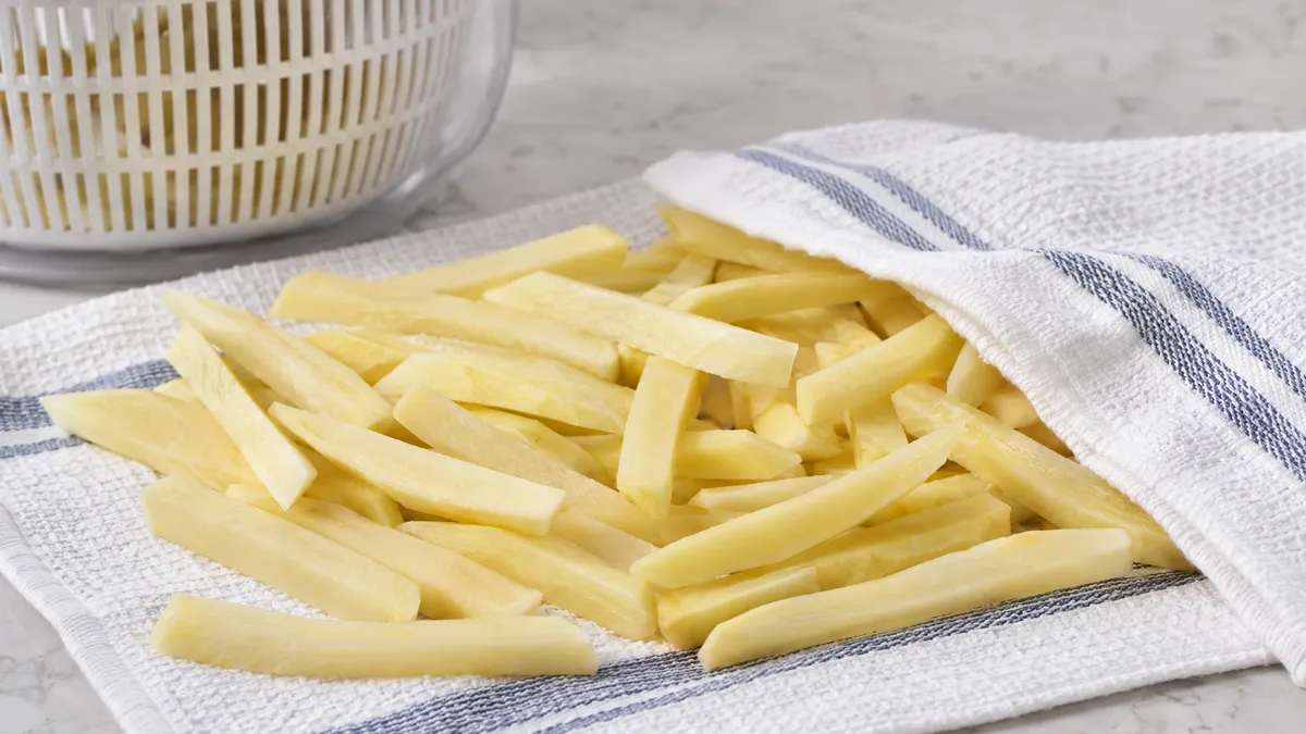 Raw cut fries spread on a clean kitchen towel to dry, with a salad spinner behind them.