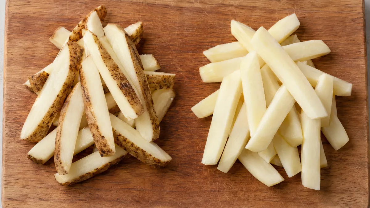 Two piles of raw cut fries on a board: skin-on fries on the left and peeled fries on the right.